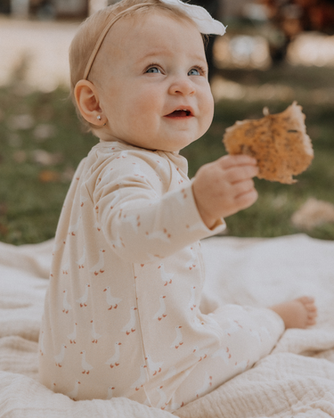 Baby wearing an organic cotton modal playsuit in geese pattern.