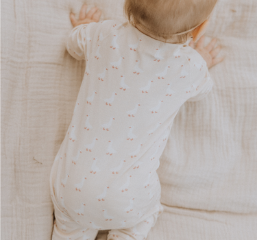 Baby wearing an organic cotton modal playsuit in geese pattern.