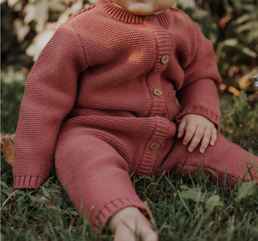 Baby girl wearing Penelope garter stitch knit organic cotton romper with magnetic button closures in rosewood pink.