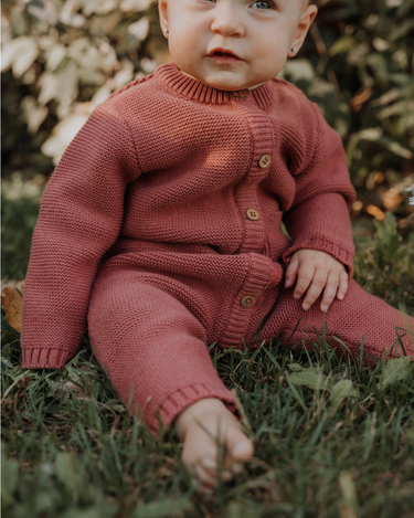 Baby girl wearing Penelope garter stitch knit organic cotton romper with magnetic button closures in rosewood pink.