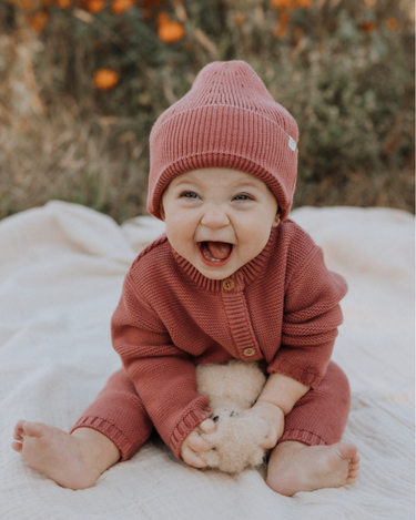 Baby girl wearing Penelope garter stitch knit organic cotton romper with magnetic button closures in rosewood pink.