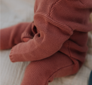 Baby girl wearing Penelope garter stitch knit organic cotton romper with magnetic button closures in rosewood pink.