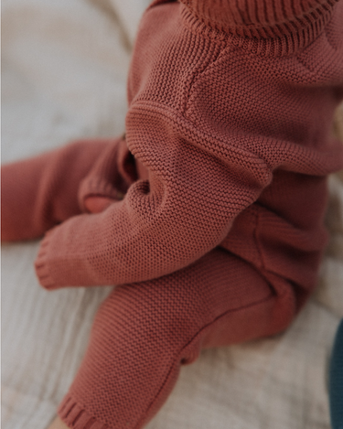 Baby girl wearing Penelope garter stitch knit organic cotton romper with magnetic button closures in rosewood pink.