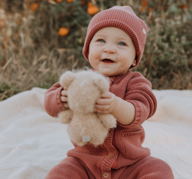 Baby girl wearing Penelope garter stitch knit organic cotton romper with magnetic button closures in rosewood pink.
