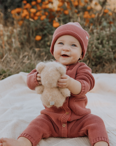 Baby girl wearing Penelope garter stitch knit organic cotton romper with magnetic button closures in rosewood pink.