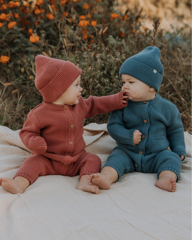 Baby girl and baby boy wearing garter stitch knit organic cotton rompers with magnetic button closures in rosewood pink and bluestone.
