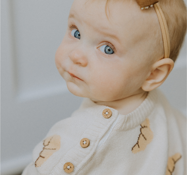 Baby girl wearing organic cotton knit croissant patterned sweater with Magnetic Button closures at the neck.