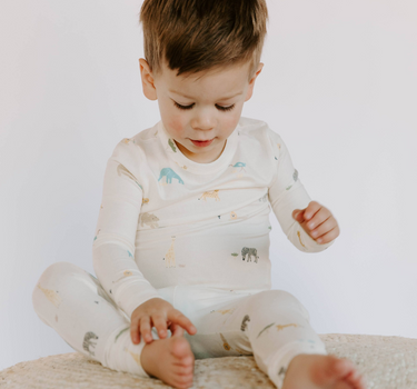 Image shows toddler boy sitting wearing modal pajama set in zoo print.
