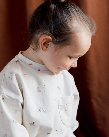 Little girl looking down wearing organic cotton Italian fleece sweatshirt in Paris print with Magnetic Buttons at shoulder. 
