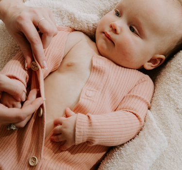 Image of baby girl wearing organic cotton rib playsuit in strawberries and cream color that opens with Magnetic Buttons for easy and struggle-free changing. 