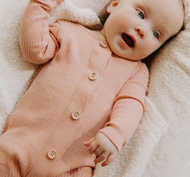 Image of baby girl wearing organic cotton rib playsuit in strawberries and cream color that opens with Magnetic Buttons for easy and struggle-free changing.