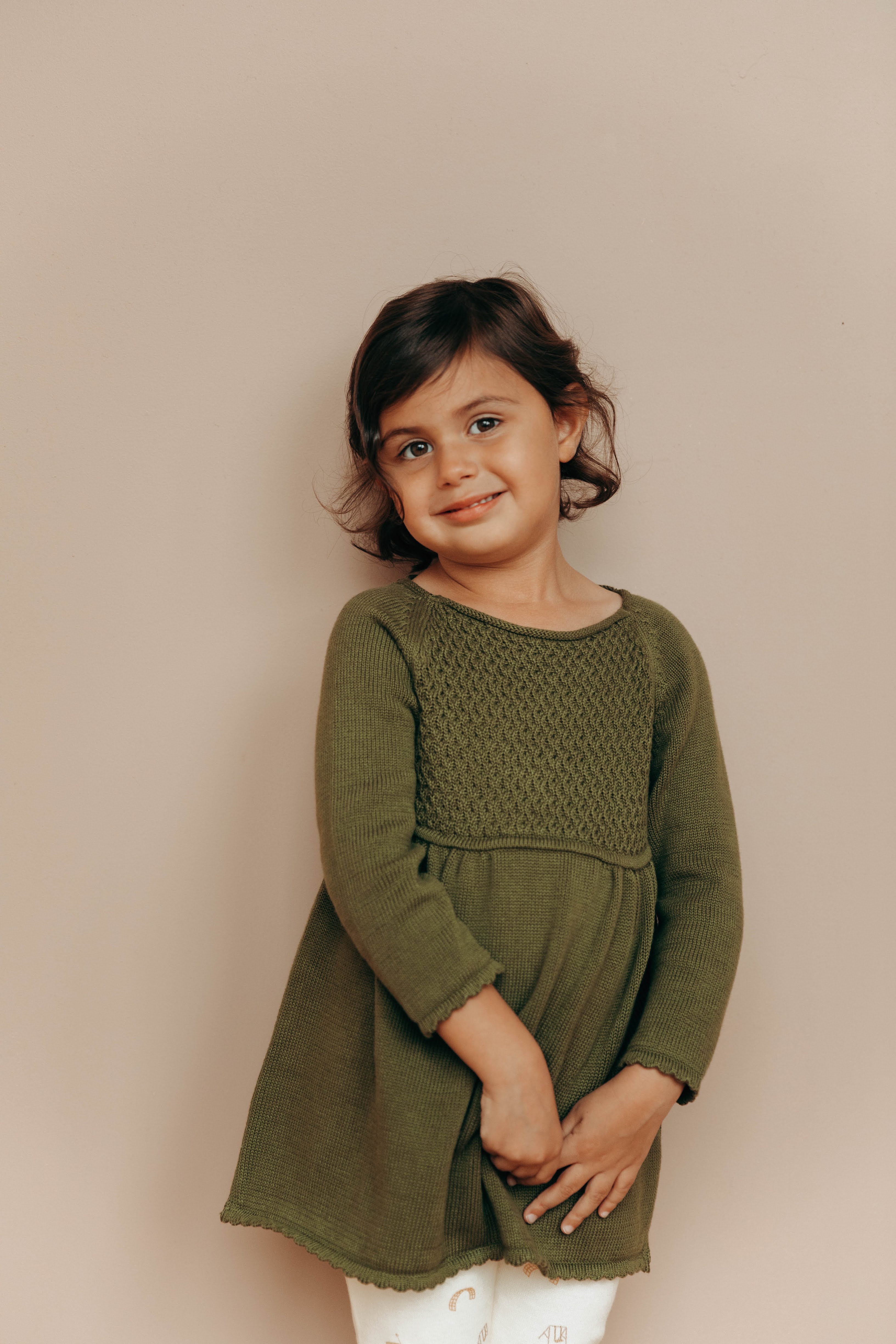 Image of little girl wearing knit dress in crocodile color with sweet details and button detail at the back of the neck. 