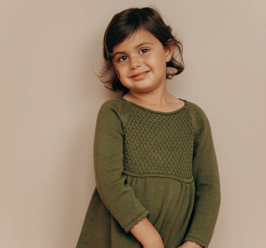 Image of little girl wearing knit dress in crocodile color with sweet details and button detail at the back of the neck. 