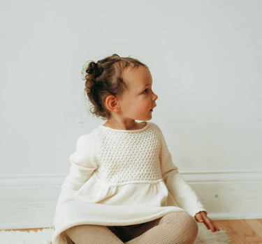 Image of little girl wearing knit dress in oatmilk color with sweet details and button detail at the back of the neck. 