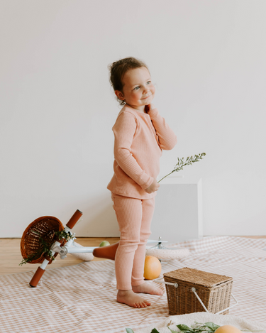 Image of little girl wearing organic cotton rib two piece set in strawberries and cream color. Set includes a long sleeve top with Magnetic Buttons at the neck in sizes through 12-18 months as well as leggings with a faux drawstring. 