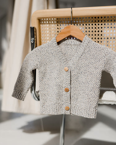 Image of organic cotton rhino gray cardigan with Magnetic Buttons hanging on hanger hanging on chair. 