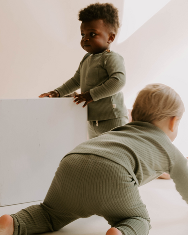 Image of little boy and baby boy wearing organic cotton rib two piece set in neutral basil color. Set includes a long sleeve top with Magnetic Buttons at the neck in sizes through 12-18 months as well as leggings with a faux drawstring.
